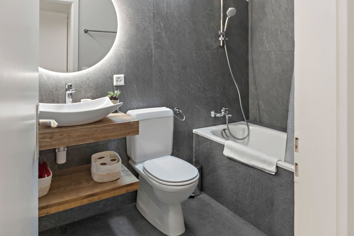 A modern bathroom with a white toilet, a wooden vanity with a sink, a large mirror, and a bathtub.