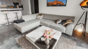 Un soggiorno moderno con un divano ad angolo grigio, un tavolino da caffè con un vaso di fiori e un quadro incorniciato di grandi dimensioni appeso al muro.