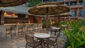 Un'area bar all'aperto con ombrelloni di paglia, pavimento in pietra e arredi in legno.