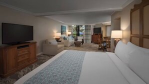 Camera d'albergo con un letto grande, una TV, una scrivania e una sedia. Si vede una finestra con vista sulle palme.