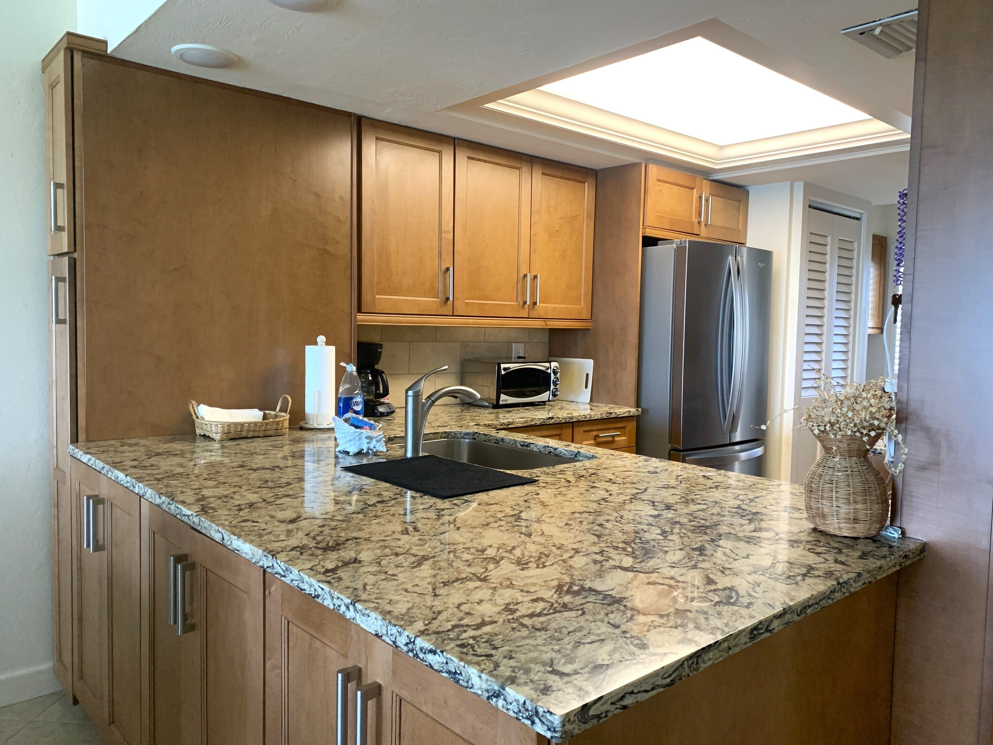 A kitchen with wooden cabinets, a granite countertop, stainless steel appliances, and a skylight.