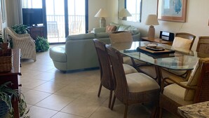 A spacious living room with a glass dining table, wicker chairs, a sofa, and a ceiling fan.