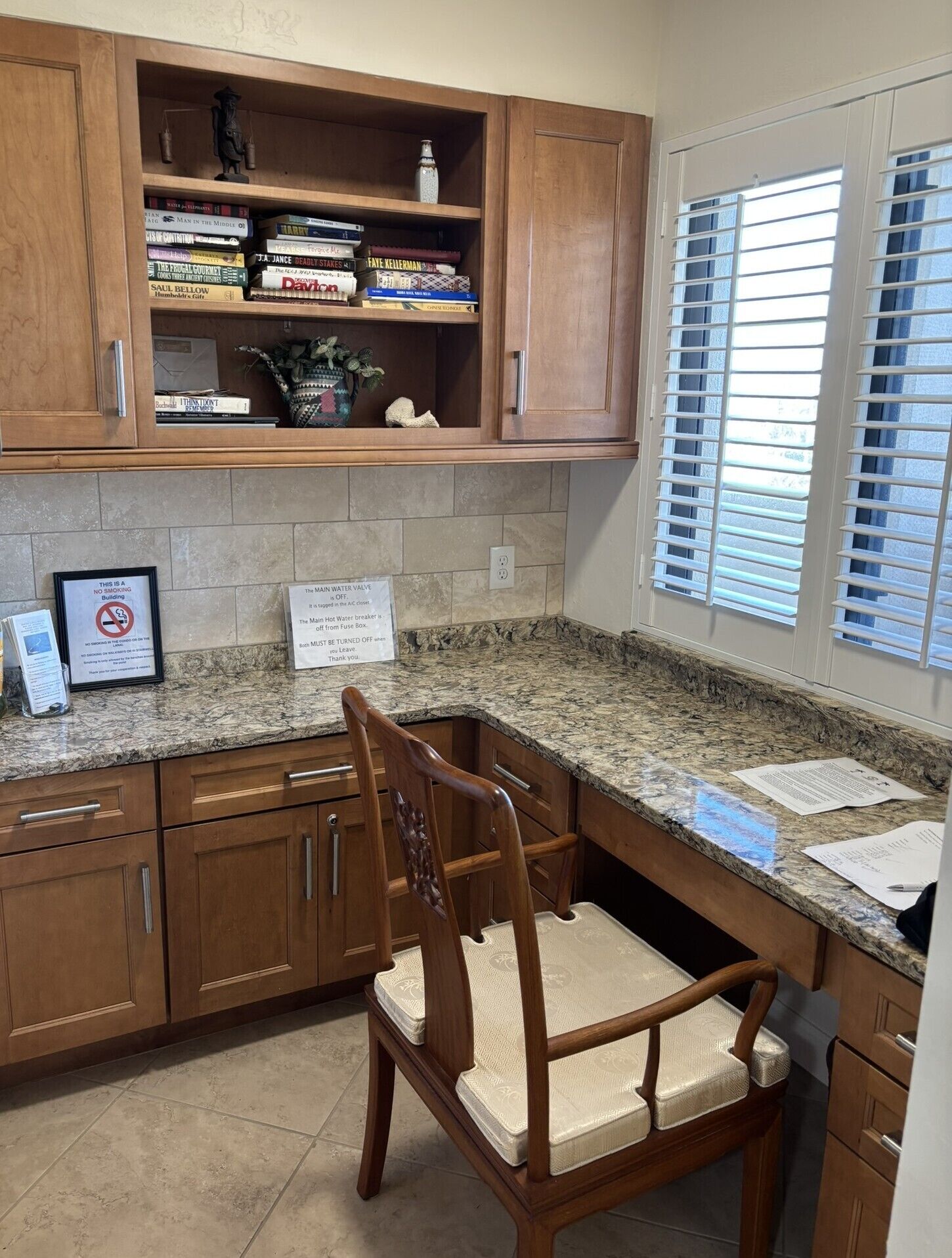 A kitchen with wooden cabinets, a granite countertop, a chair, and a window with blinds.