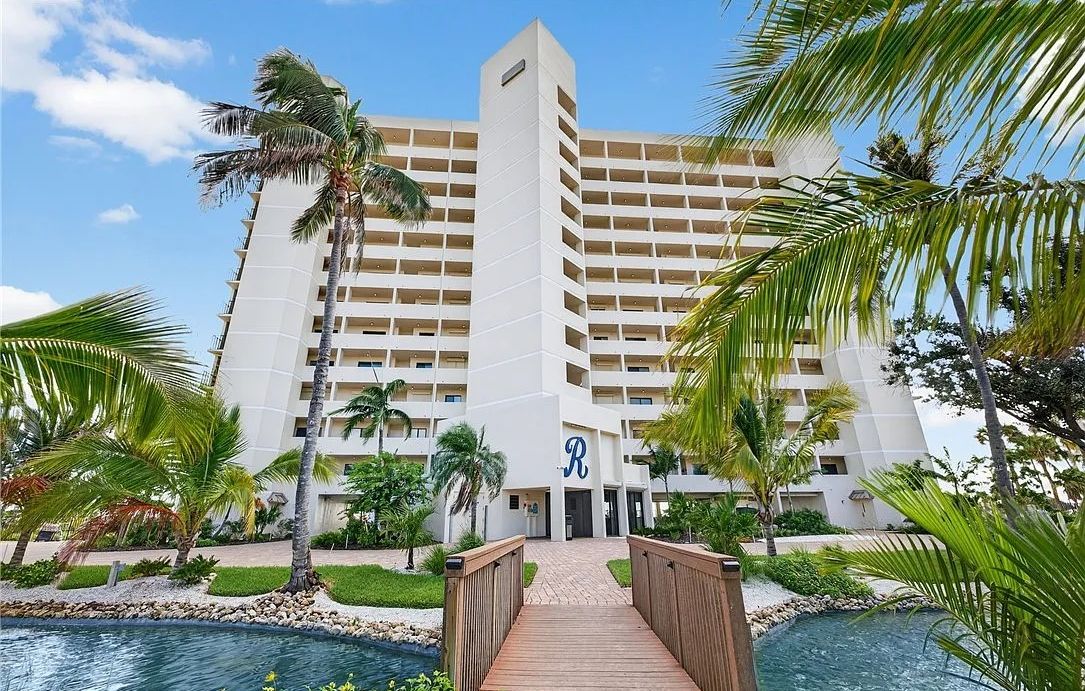 A hotel with a central tower, a pool, and a wooden bridge.