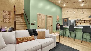 A modern interior with a light-colored sofa, a kitchen area, and a staircase. - Modern Cabin Retreat w/ Hot Tub, Fire Pit & Arcade near Pigeon Forge - Pets OK (Sevierville)