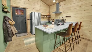 A compact kitchen with wooden walls, a marble countertop, and a central island with bar stools. - Modern Cabin Retreat w/ Hot Tub, Fire Pit & Arcade near Pigeon Forge - Pets OK (Sevierville)