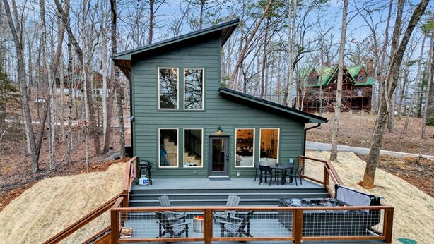 A two-story cabin with a deck, surrounded by trees. - Modern Cabin Retreat w/ Hot Tub, Fire Pit & Arcade near Pigeon Forge - Pets OK (Sevierville)