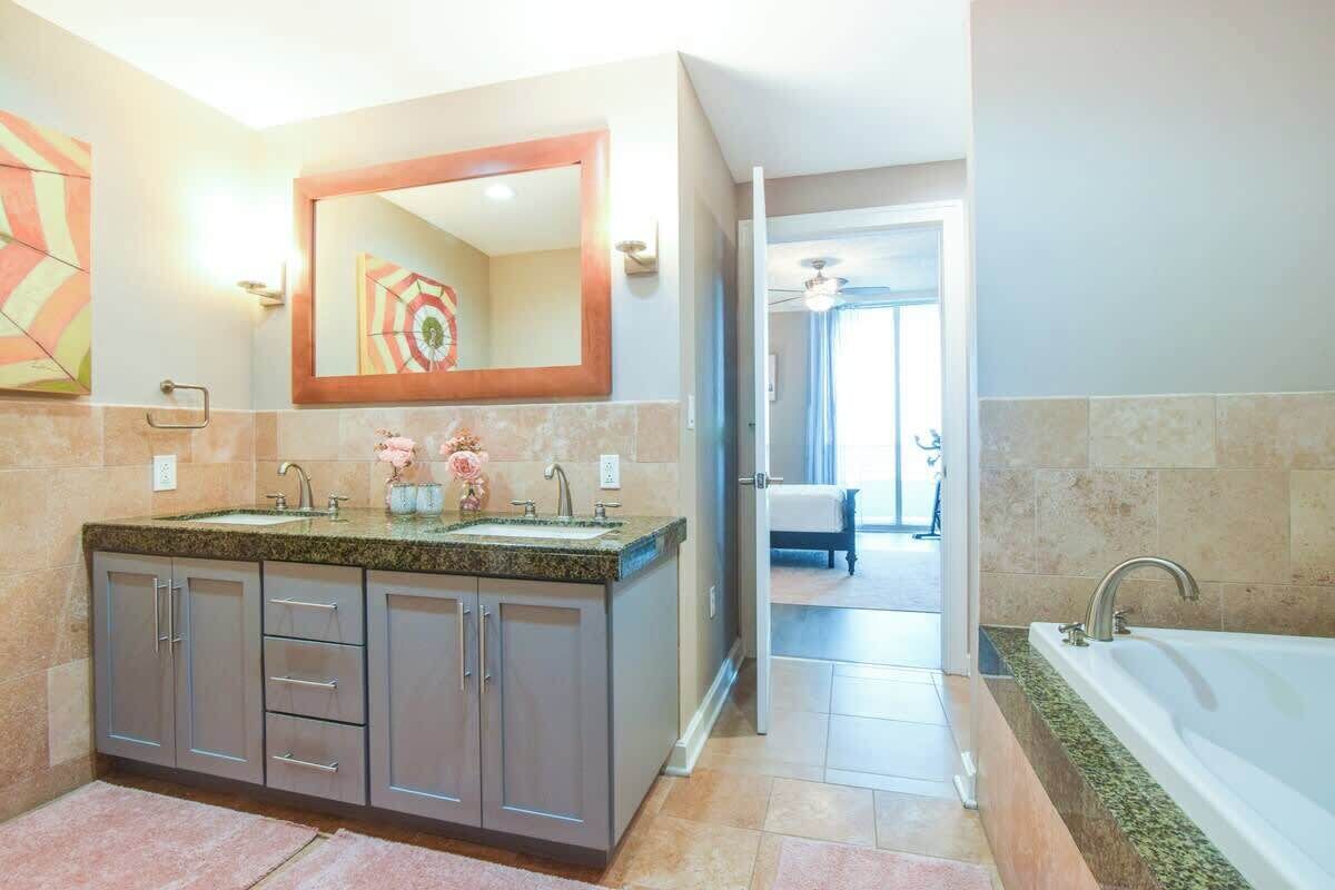 Une salle de bain moderne avec un lavabo surmonté d’un plan de travail en granit, un grand miroir et une baignoire séparée.
