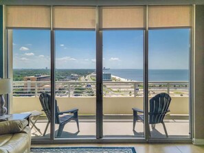 A balcony with two chairs, a sofa, and a view of the ocean and cityscape. - Beautiful 15th Floor 2 Bedroom, 2 Bath Condo at The Ocean Club! (Biloxi)