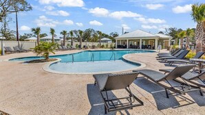 A pool area with lounge chairs and a building in the background. - Luxury Pondside Retreat (Murrells Inlet)