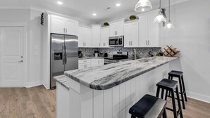 A modern kitchen with white cabinets, a marble countertop, stainless steel appliances, and pendant lighting. - Luxury Pondside Retreat (Murrells Inlet)