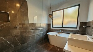 A modern bathroom with a freestanding bathtub, a vanity with a sink, and a large window providing natural light. - Snapper Hideaway - Pet Friendly (Merimbula)