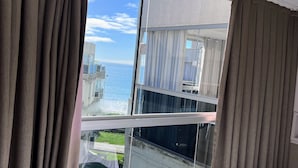 A view through a window with curtains, overlooking a building with a balcony and a clear sky. - Apartamento Itapema (Itapema)