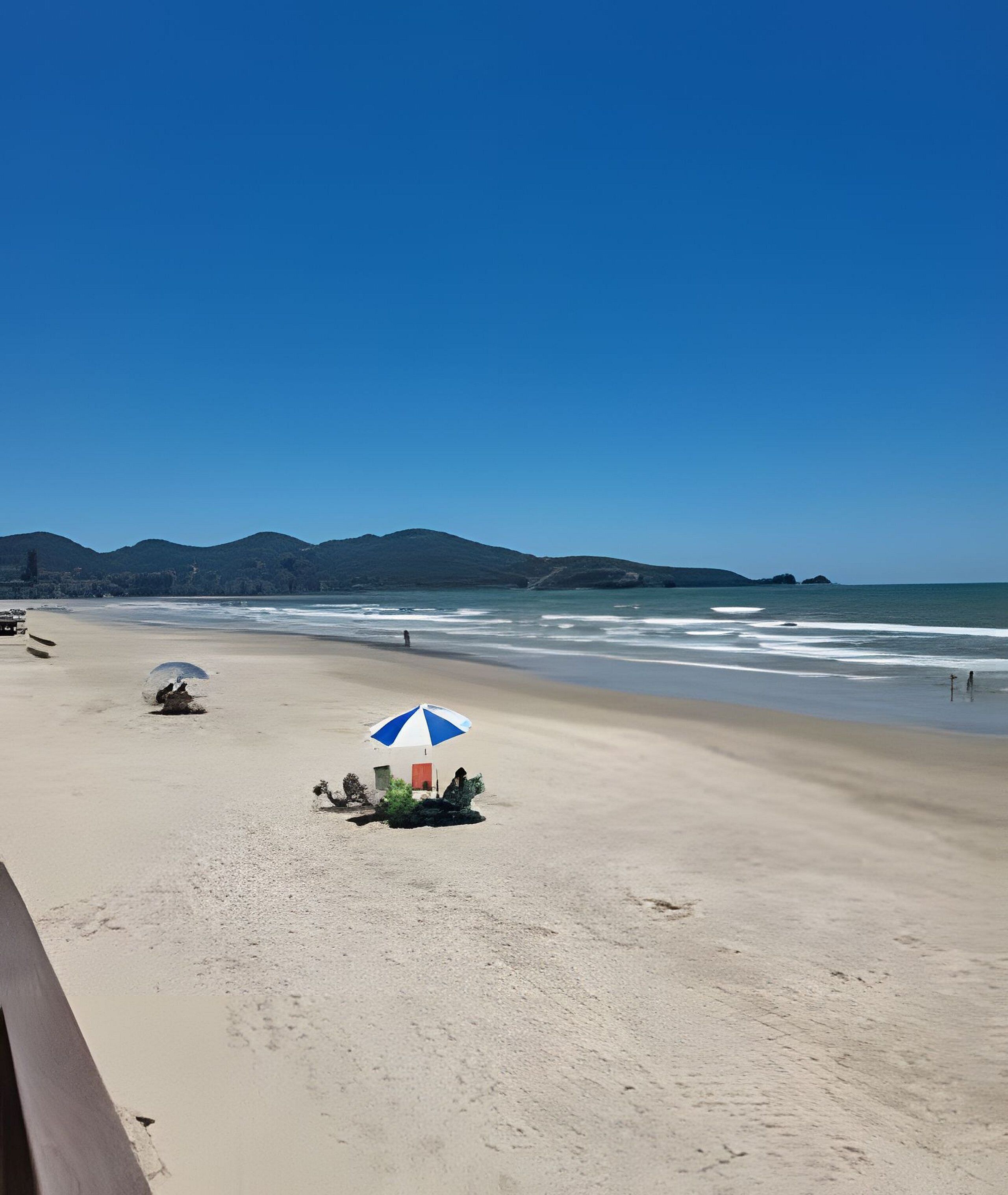 Una playa con una pequeña estructura y un paraguas azul y blanco.