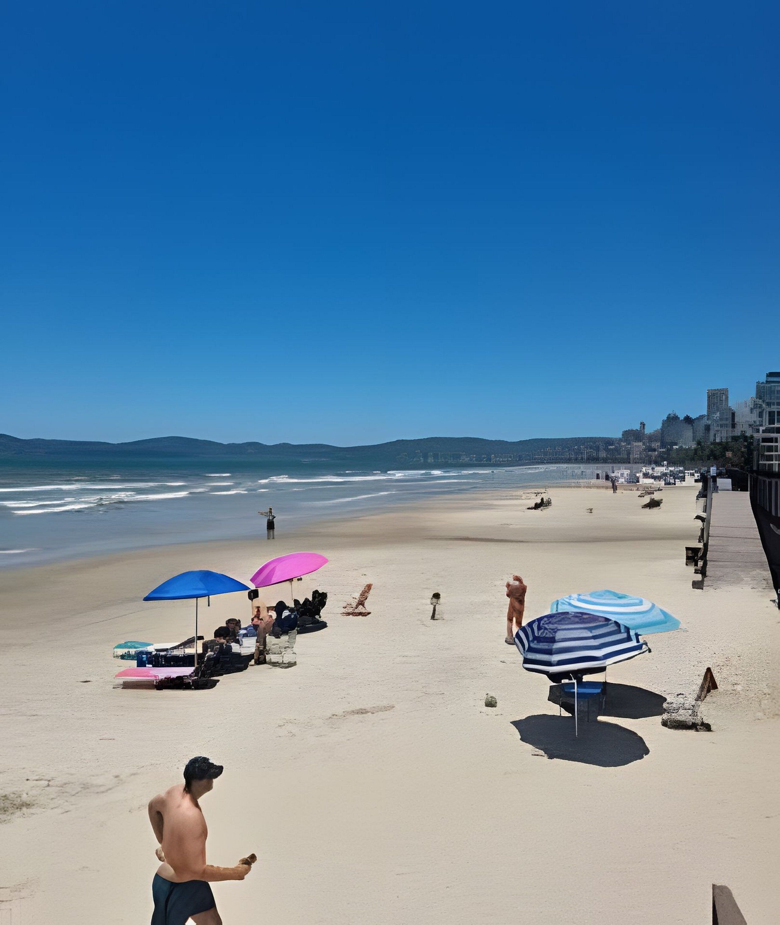 Une plage avec des parasols, des gens et une vue sur la ville en arrière-plan.