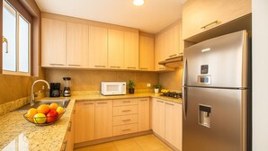 Una cocina moderna con armarios de madera, un refrigerador de acero inoxidable, un microondas y un frutero en la encimera.