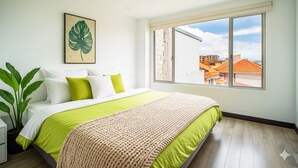 Un dormitorio con una cama grande, vistas a edificios a través de una ventana y una planta en maceta.