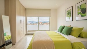 Un dormitorio con cama, espejo y vista a la ciudad.