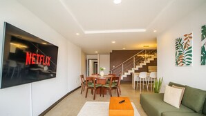 Una sala moderna con televisor de pantalla plana, comedor, escalera y sofá verde.