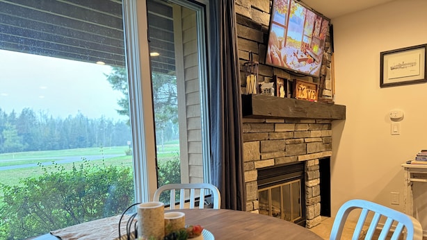 A dining area with a table set for two, a fireplace, and a large window overlooking a green landscape.