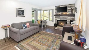 A living room with a gray sofa, a patterned rug, a fireplace, and a television mounted on the wall.