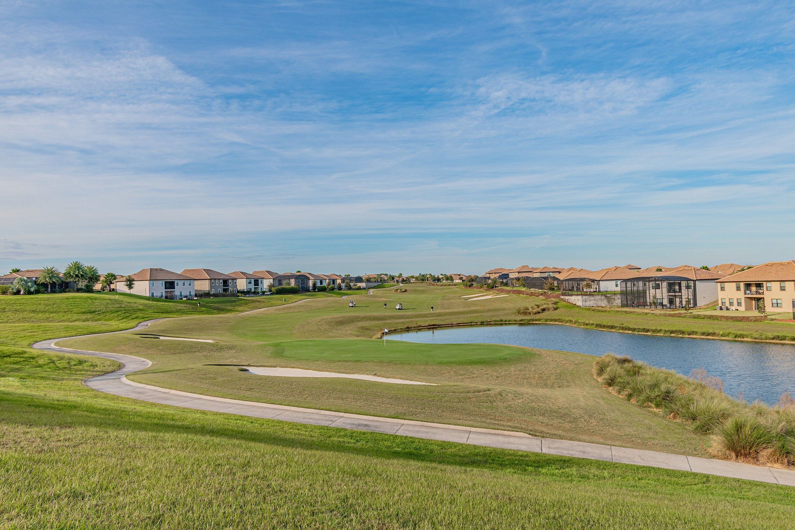 Un campo de golf con un estanque, rodeado de edificios residenciales.
