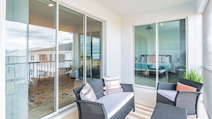 A balcony with wicker furniture, a glass door leading to a bedroom, and a view of the outdoors.