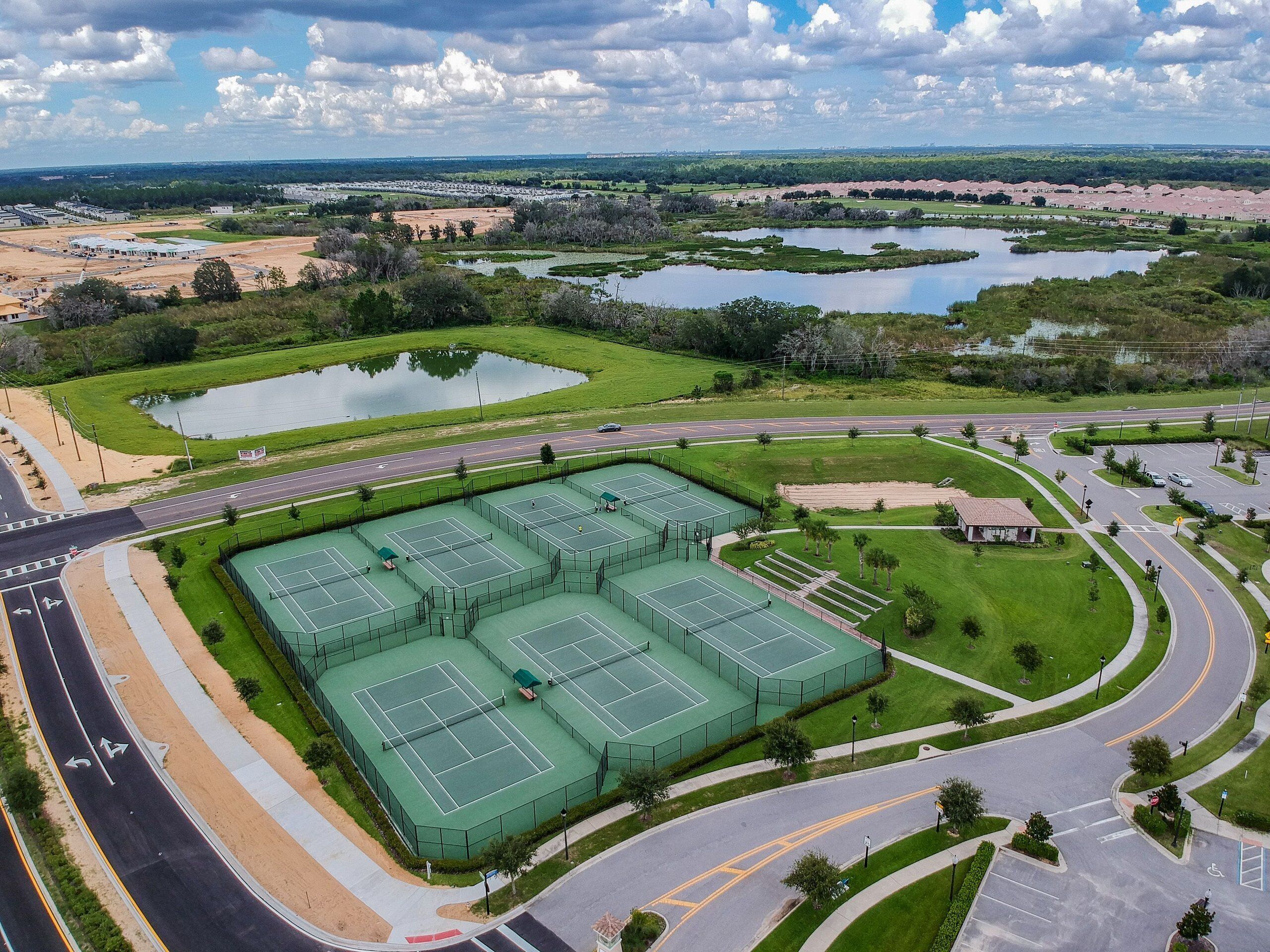 A large sports complex with multiple tennis courts, a parking area, and surrounding green spaces.