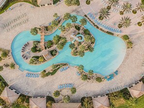 An aerial view of a resort with a winding pool, sun loungers, and palm trees. - Champions Gate 3BR Retreat Near Disney (Davenport)