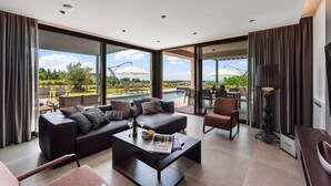 A modern living room with a sofa, coffee table, and a dining area with chairs and a table. There is a large window with a view of a pool and outdoor furniture. - Villa Visignano with heated pool and welness facilities (Višnjan)