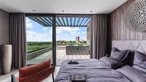 A modern bedroom with a large bed, a bench, and a view of a cityscape through a glass door. - Villa Visignano with heated pool and welness facilities (Višnjan)