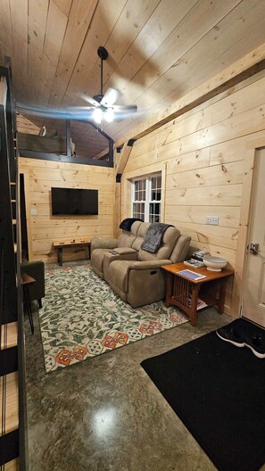 A cozy living room with a sectional sofa, a flat-screen TV, a ceiling fan, and a patterned rug.