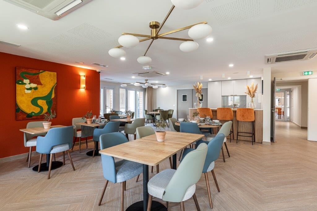 A modern dining area with wooden tables and chairs, a decorative ceiling light, and a large abstract painting on the wall.