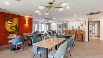 A modern dining area with wooden tables and chairs, a decorative ceiling light, and a large abstract painting on the wall.