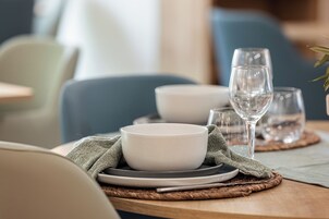 Una mesa de comedor dispuesta con cuencos, platos y vasos blancos sobre individuales tejidos.
