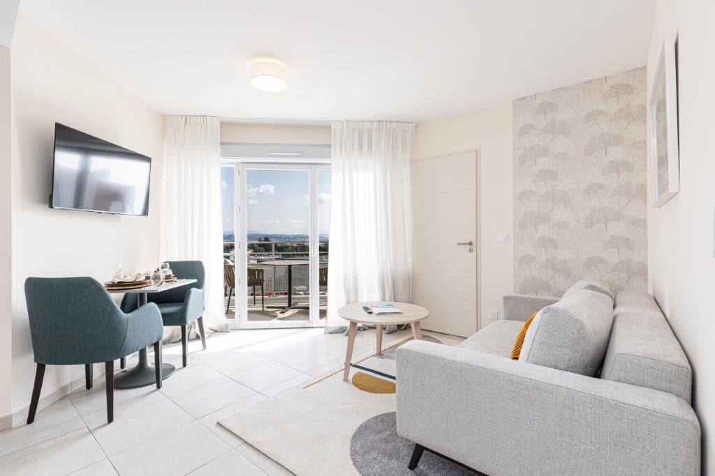 A modern living room with a grey sofa, teal chairs, a flat-screen TV, and a balcony with a city view.