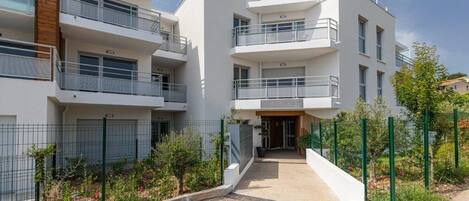 A modern multi-story residential building with balconies, a gated entrance, and a landscaped garden area.