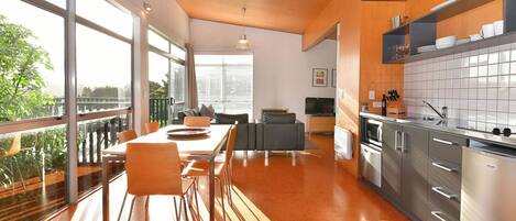 A modern kitchen with large windows, a dining area with a table and chairs, and a kitchen island.