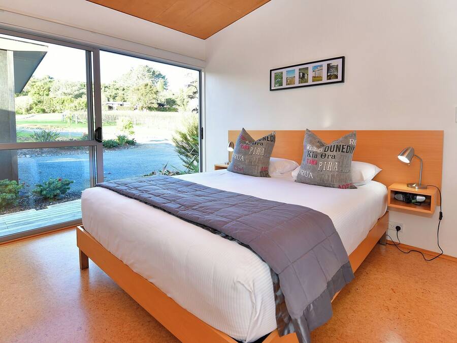 Une chambre moderne avec un grand lit, une tête de lit en bois et une vue sur un jardin, accessible par une porte-fenêtre coulissante.