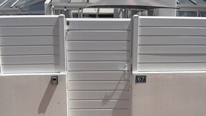 Una entrada tancada per una reixa metàl·lica, amb un senyal que indica el número 67 i una paret amb una petita caixa elèctrica.