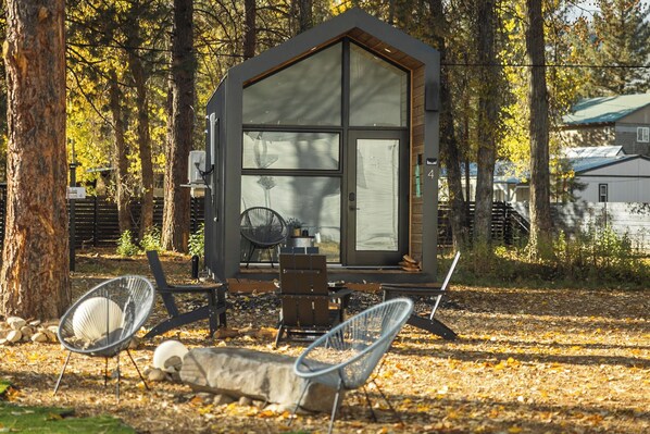 Eine Holzhütte mit großem Fenster, einem Sessel und einem Tisch in einem bewaldeten Gebiet.