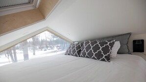 Ein Schlafzimmer mit Oberlicht, einem Bett mit gemusterten Kissen und einem Nachttisch mit Lampe.