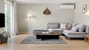 A modern living room with a grey sofa, a coffee table, and a TV on the left. - Cozy country house with outdoor pool (Kalvehave)
