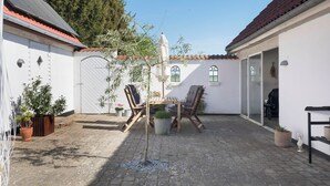 A courtyard with a table and chairs, surrounded by potted plants and a white building with a tiled roof. - Cozy country house with outdoor pool (Kalvehave)