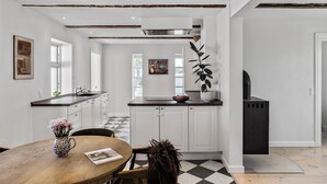 A modern kitchen with white cabinets, a black countertop, and a dining area with a wooden table and chairs. - Cozy country house with outdoor pool (Kalvehave)