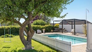 A backyard with a swimming pool, a wooden deck, and a covered seating area. - Cozy country house with outdoor pool (Kalvehave)