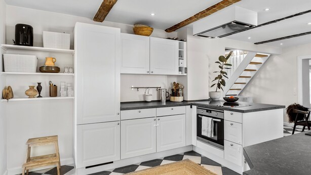 A modern kitchen with white cabinetry, a black and white checkered floor, and a wooden ceiling beam. - Cozy country house with outdoor pool (Kalvehave)