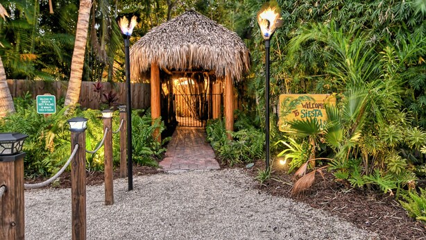 A pathway leading to a thatched-roof structure with a sign welcoming visitors to Siesta Key. - Siesta Key Palms Hotel - Gran Studio (Sarasota)