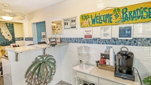A reception area with a 'Welcome to Paradise' sign, a water dispenser, a coffee maker, and a reception desk with a map and framed pictures on the wall. - Siesta Key Palms Hotel - Gran Studio (Sarasota)