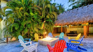 An outdoor seating area with Adirondack chairs, a fire pit, and a thatched-roof structure. - Siesta Key Palms Hotel - Gran Studio (Sarasota)